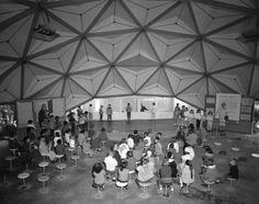 an old photo of people sitting at tables in a large room with lots of windows