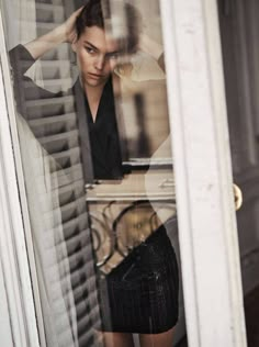 a woman standing in front of a window with her hand on her head