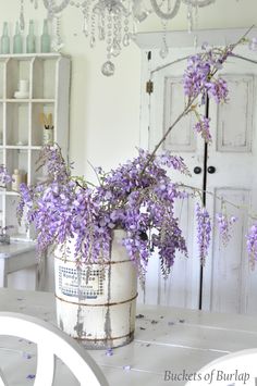 a white bucket with purple flowers in it on top of a table next to a door