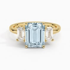 Aquamarine Luxe Rhiannon Three Stone Diamond Engagement Ring (3/4 ct. tw.) - 18K Yellow Gold. Two luxurious emerald-cut diamonds rest alongside the center gemstone in this classic, sophisticated ring (3/4 total carat weight). Earth Engagement Rings, Emerald Cut Aquamarine Ring, Aquamarine Cocktail Ring, Moissanite Engagement Ring Rose Gold, Three Stone Diamond Rings Engagement, Three Stone Diamond Ring, Stone Diamond Ring, Yellow Gold Wedding Ring, Emerald Cut Rings