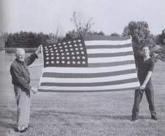 two people holding an american flag in the grass