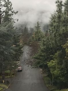 a car driving down a road surrounded by trees and fog in the distance with low lying clouds