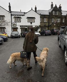 a woman walking two dogs on a leash in the middle of a parking lot next to parked cars