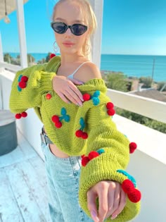 a woman wearing a green sweater with red and blue pom poms on it