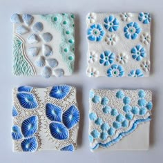 four small blue and white tiles are shown on a table top, one is made out of clay