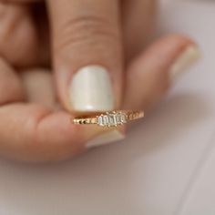 a woman's hand holding a gold ring with three diamonds on it and a white manicure