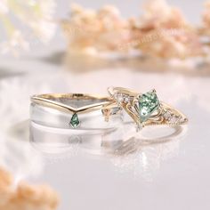 two wedding rings with green and white stones on them sitting on a table next to flowers