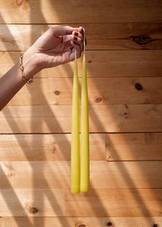 a hand holding two yellow candles in front of a wooden wall with wood planks