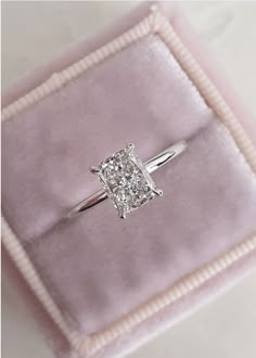 a diamond ring sitting on top of a pink velvet cushioned box with a white ribbon around it