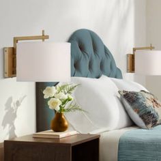 a bed with white pillows and blue headboard next to a night stand with flowers on it