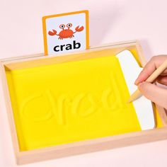 a child's hand holding a pencil in front of a yellow eraser with the word crab on it