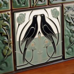 two black birds sitting on top of a wooden table next to tile panels with flowers and leaves