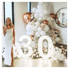 a woman standing in front of balloons that spell out the number thirty and there are flowers