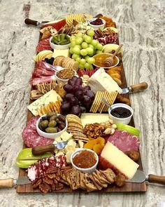 a platter filled with cheese, crackers, grapes and olives on a marble table