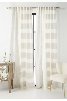 a white chair sitting in front of a window next to a wooden table and curtain