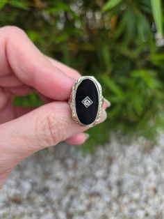 a person is holding a ring with a black stone in front of some grass and bushes