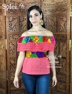 a woman standing in front of a wooden door wearing a pink top with colorful flowers on it