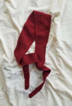 a red knitted headband laying on top of a white bed sheet with a knot at the end