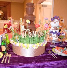 a table topped with a cake covered in grass and flowers next to a chocolate fountain