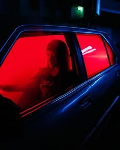 a man sitting in the back seat of a car with red light coming from his window