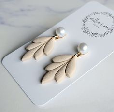 two pairs of earrings with leaves and pearls on top of a white tray next to a card