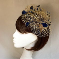 Delicate gold and navy fascinator perfect for the guest who wants something fairly understated. This design is a beautiful selection of glass effect leaves and flowers clustered together amongst a fine layer of veiling and set onto a gold ribbon base tiara band.As with all our designs, this piece can be made in any colour combination and set onto either a band or a comb which you can state either before or after orderingAs a online shop item this item can be made exact to the sample in the pictu Gold Crown Costume Headpiece For Weddings, Gold Party Hair Accessories With Structured Crown, Gold Headpiece With Round Crown For Party, Gold Round Crown Headpiece For Party, Gold Hair Accessories With Structured Crown For Party, Gold Fascinator For Kentucky Derby Event, Gold Headpieces For Royal Ascot Formal Occasion, Gold Mini Hat For Royal Ascot Event, Gold Crown Headpiece For Evening