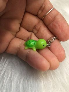 a tiny green turtle necklace is being held in someone's hand