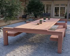 a wooden table sitting in the middle of a gravel covered yard with potted plants on it