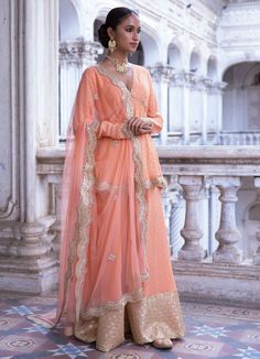 This look features a tangerine banarasi kurta sharara set. The georgette Benarasi kurta is a v neck, with full sleeves, empire cut and circular ghera. It is embellished with mirror, pearl and scallop gold laces. Teamed with a matching sharara with broad gold embroidery border. A matching net dupatta with a scallop border and bootis completes the look. Composition: Kurta - Viscose georgette Sharara-Viscose georgette Dupatta - Soft net Care: Dry Clean Only and Vacuum Storage This product can be customised for colour, sleeves, length of blouse and neck design Delivery : 2 weeks as the product is hand crafted. For more information and sizes please contact fabiliciousfashion@gmail.com or visit our Copenhagen studio. About the Designer : Renee Label was created in 2013,by the talented sister duo Long Sleeve Lehenga With Gota Work For Eid, Orange Chikankari Embroidery Palazzo Set For Designer Wear, Orange Chikankari Embroidery Palazzo Set, Anarkali Palazzo Set With Zari Work And Long Sleeves, Orange Palazzo Set With Straight Kurta For Wedding, Orange Wedding Palazzo Set With Straight Kurta, Orange Semi-stitched Palazzo Set For Eid, Eid V-neck Sets With Zari Work, Traditional V-neck Set With Sheer Dupatta