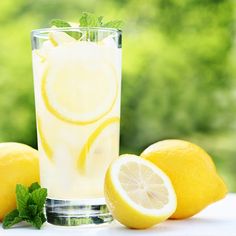 a glass filled with lemonade sitting next to two lemons and mint sprigs