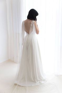 the back of a woman's wedding dress in front of a window with sheer curtains