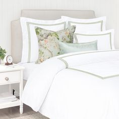 a bed with white sheets and green trimmings on the headboard is next to a night stand