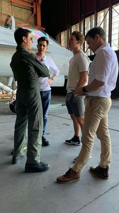 four men are standing in front of an airplane and talking to each other while another man stands nearby