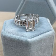 an emerald cut diamond ring sitting on top of a blue velvet box