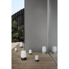 four white lamps sitting on top of a wooden table next to a tall building and trees