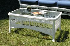 a white wicker coffee table sitting on top of a green grass covered field next to a blue couch