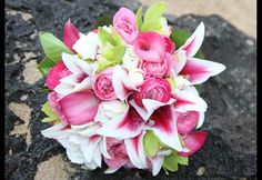 a bridal bouquet with pink and white flowers on the ground in front of some rocks