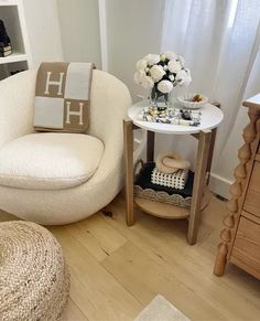 a white chair sitting next to a small table with flowers on it and a vase