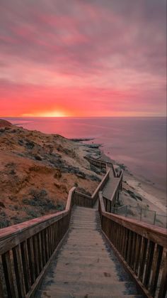 stairs leading down to the beach at sunset with pink and orange clouds in the background