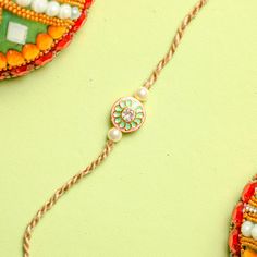 This year, on rakshabandhan, express your emotions and love with an exclusive Kundan rakhi for brother. Designed with a Kundan pendant of 1 inch, this elegant rakhi displays a round shape. It has a white stone at the center, surrounded by pink and green design. Off-white beads and beige threads complete the look of this rakhi. Order this elegant rakhi today. Yellow Gold Bracelet For Festive Gift, Festive Yellow Gold Bracelets For Gifts, Yellow Gold Meenakari Bracelets As Gift, Fusion Style Bracelets As Festival Gifts, Temple Jewelry Bracelets As Gift, Temple Jewelry Bracelet As Gift, Round Pendant Jewelry For Festivals And Gifts, Festive Fusion Style Bracelets As Gift, Festive Fusion Style Bracelet For Gift