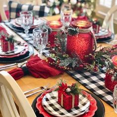 a table set for christmas dinner with red and black plates, plaid napkins and candles