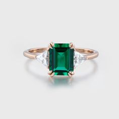 an emerald and diamond ring with three diamonds on the band, set in 18k rose gold