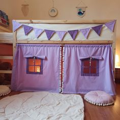 a bed with purple curtains and pillows on it's sides, next to a teddy bear