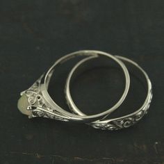 two silver rings sitting next to each other on top of a black surface with an oval stone in the middle