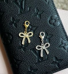 two pairs of earrings with bows hanging from them on top of a black case next to a wallet