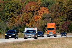 three trucks driving down the road with trees in the background and grass on both sides