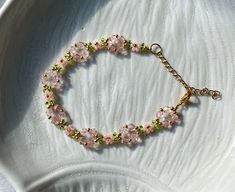 a bracelet with pink flowers and green beads on a white plate next to a spoon