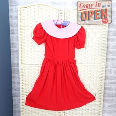 a red dress hanging on a wall next to a white wicker chair and sign