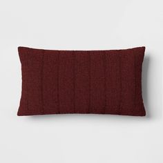 a red pillow on a white wall with a dark brown corded material behind it