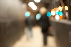 blurry image of people walking down a sidewalk at night time with lights in the background